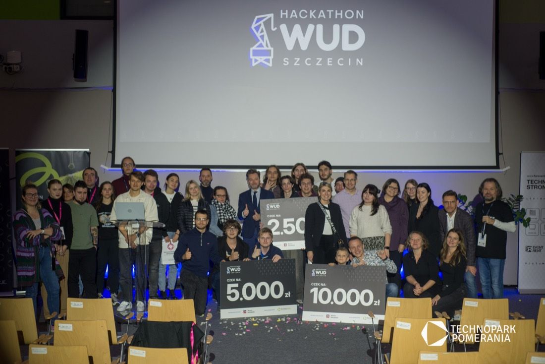 Wspólne zdjęcie uczestników hackathonu z czekami na scenie